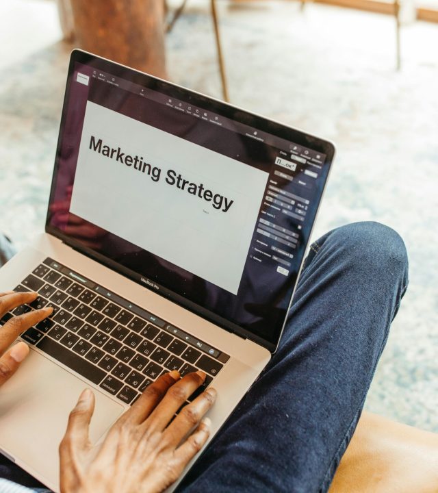 Close-up of hands using a laptop displaying a marketing strategy presentation indoors.